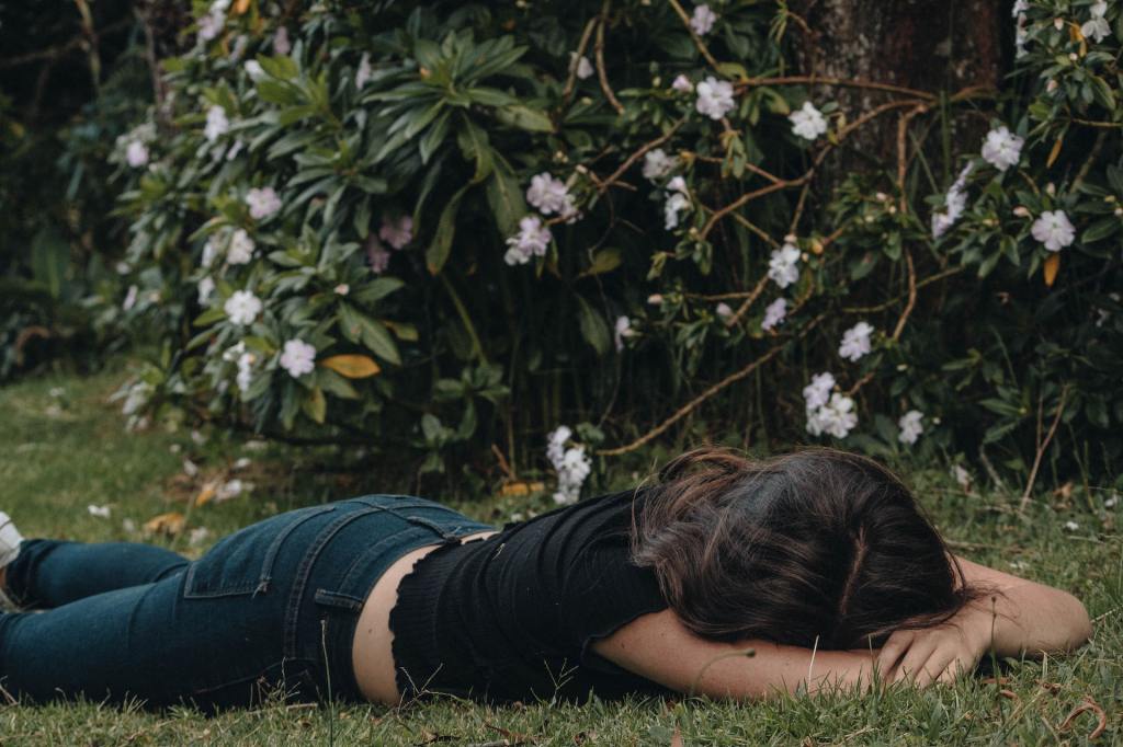 A woman lies face down in the grass with her arms around her head.